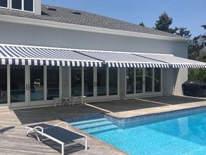 An open Sunesta awning provides shade beside a backyard pool in the Northeast